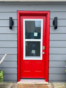 A vibrant red door from EcoTech adds a bold, welcoming touch to the home's entrance, perfect for a summer refresh.