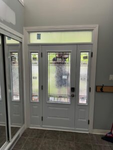 White front door with a transom window above and narrow sidelights on either side, allowing natural light to enter the entryway.